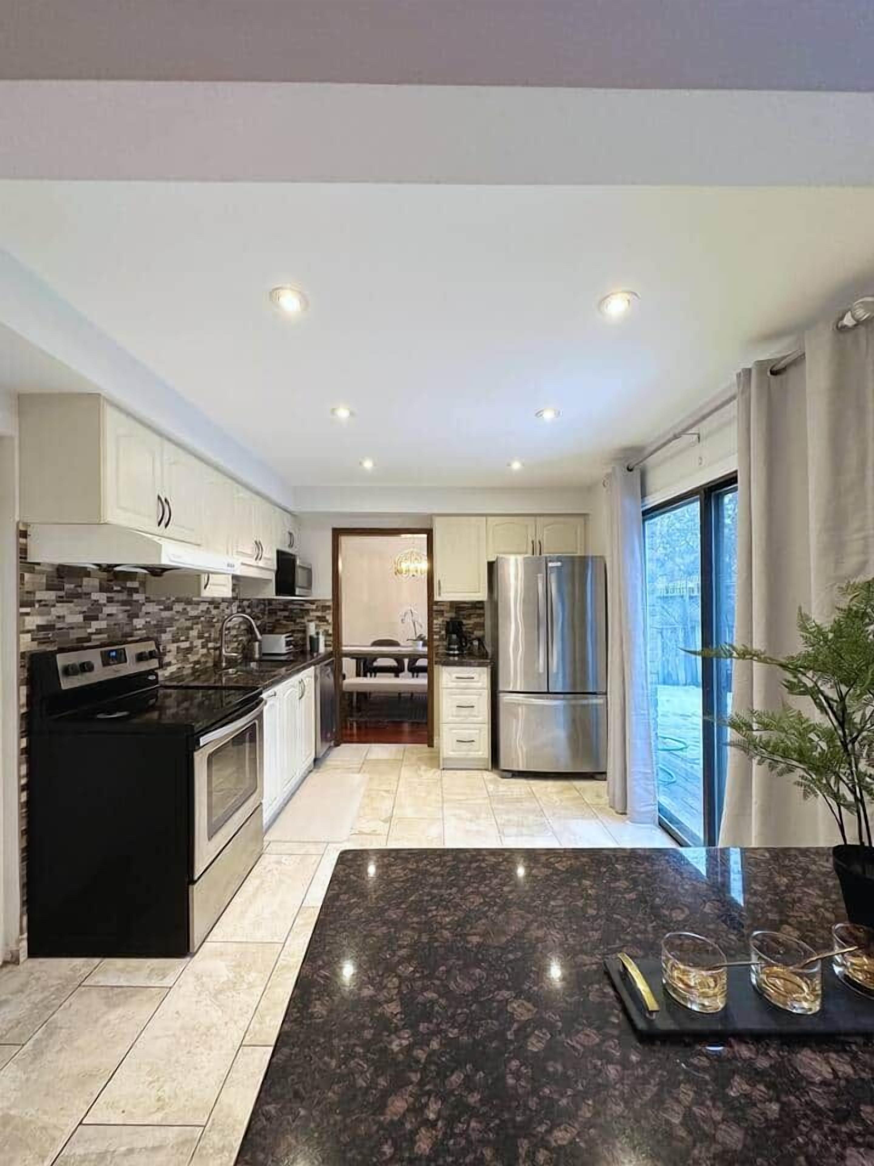 A modern kitchen with a central island, stainless steel appliances, and a view to the outside.
