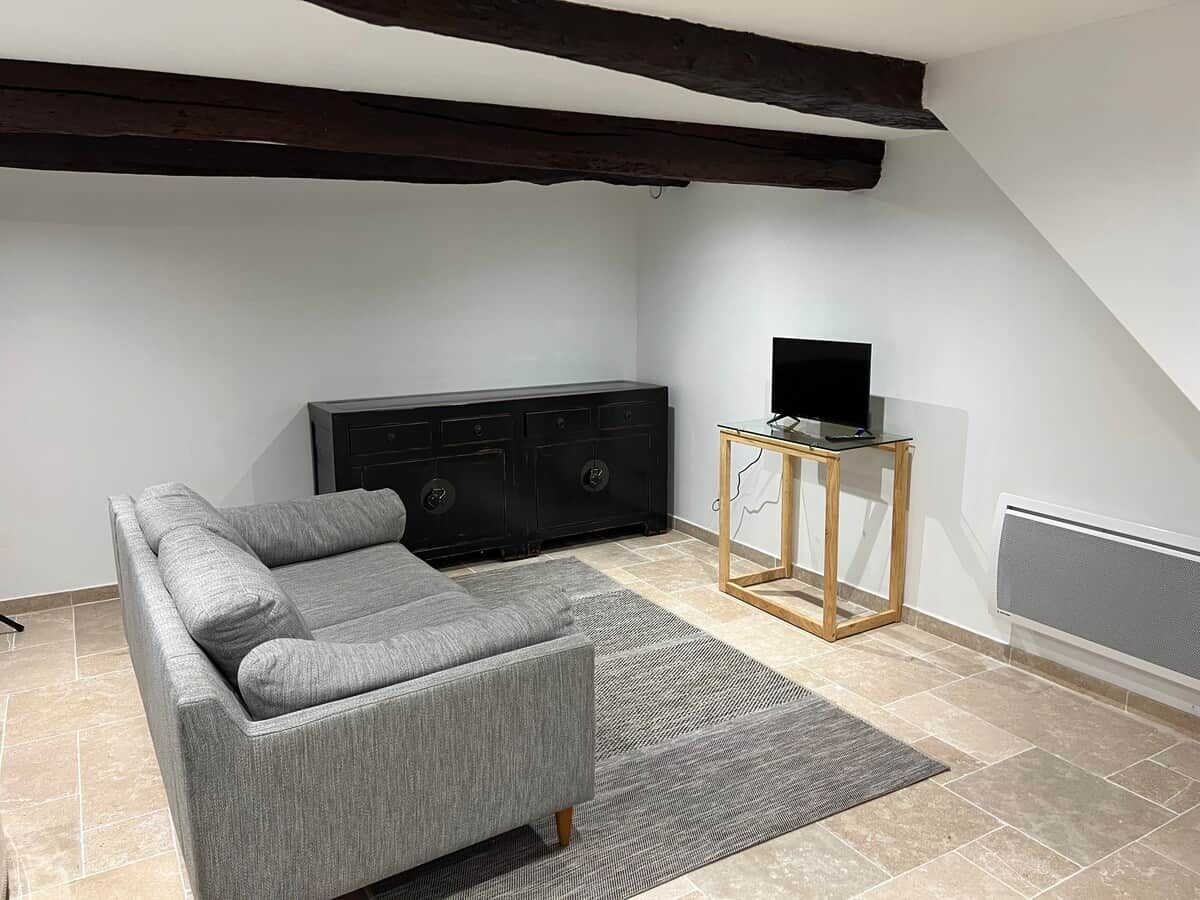 Un salon moderne avec un canapé gris, un meuble de rangement noir pour appareils électroniques et une petite table d’appoint en bois.
