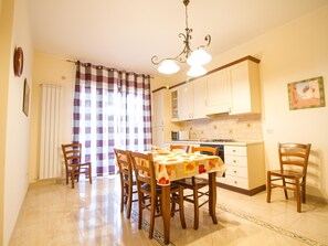 A dining area with a table set for four, wooden chairs, a chandelier, and a kitchen in the background. - Sea-view Etna Residence (Trecastagni)