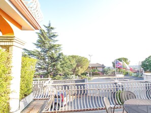 A balcony with a metal railing, a car parked in the background, and a flagpole with flags. - Sea-view Etna Residence (Trecastagni)