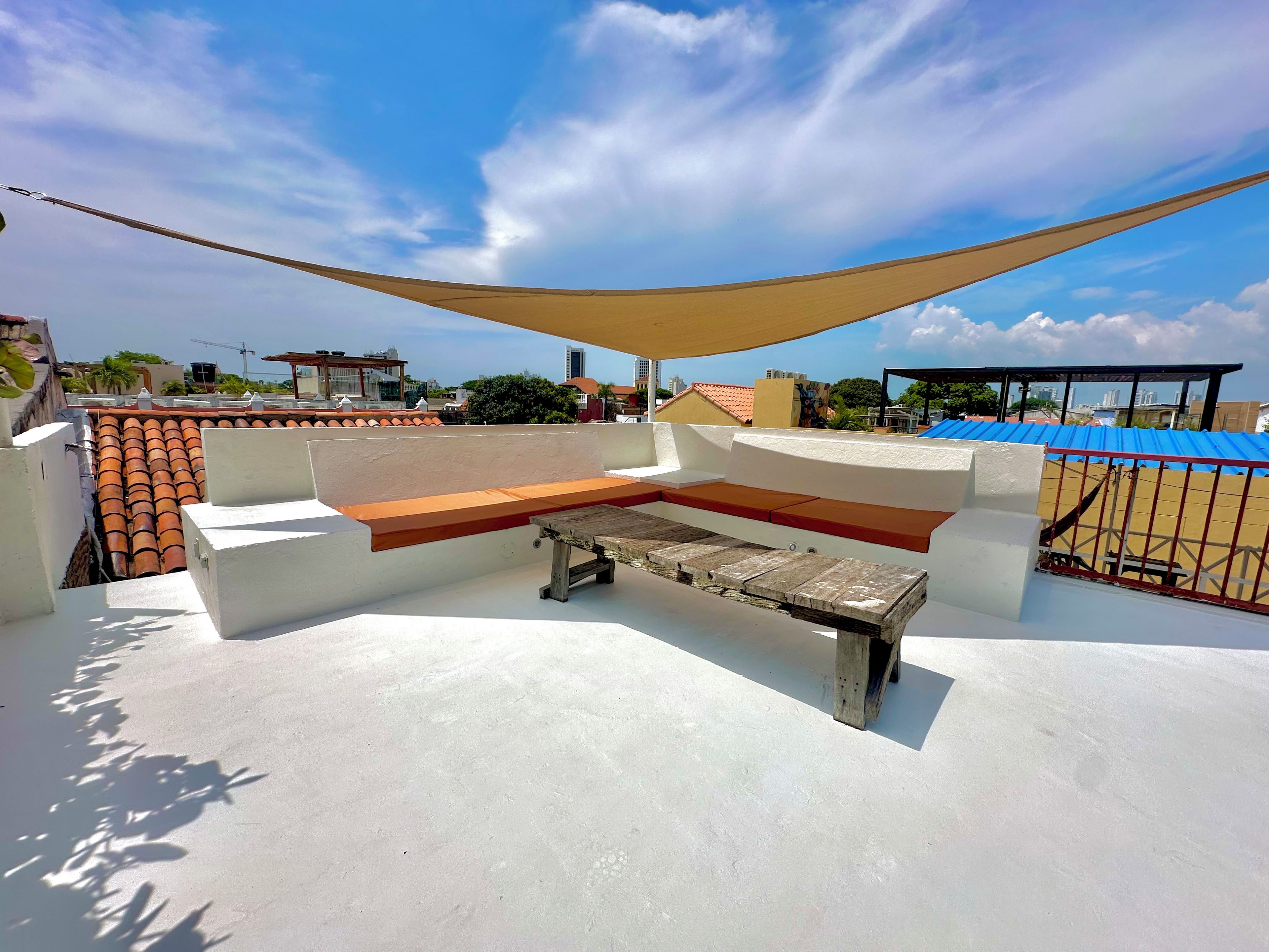 Una terraza en la azotea con zona de estar, una mesa y una vela de sombra.