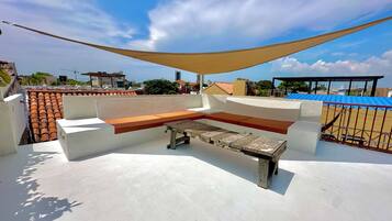 Una terraza en la azotea con zona de estar, una mesa y una vela de sombra.