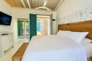 Une chambre avec un grand lit, un ventilateur de plafond, une télévision et une vue sur l’extérieur.