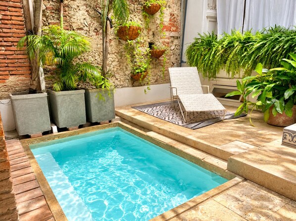 A rectangular pool with clear blue water, surrounded by potted plants and a white lounge chair. - by Calamari.Homes - Casa Aura Victoria - Visitors permitted (Cartagena de Indias)