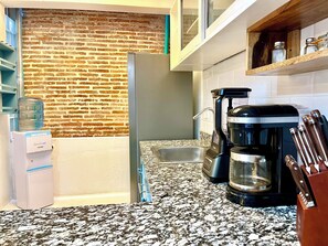 Et køkken med en murstensvæg, en vanddispenser, kaffemaskine og et knivdisplay.
