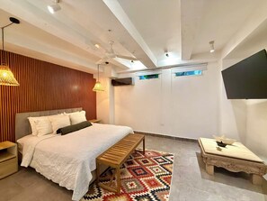 A modern bedroom with a bed, a wooden bench, a patterned rug, and a TV mounted on the wall. - by Calamari.Homes - Casa Aura Victoria - Visitors permitted (Cartagena de Indias)