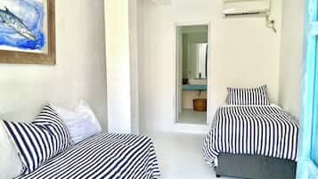 Una habitación con dos camas, un cuadro, y un baño visible a través de una puerta abierta, además de un equipo de aire acondicionado.