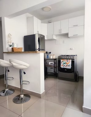 A modern kitchen with white cabinets, a black refrigerator, a gas stove, and two bar stools. - Fully Furnished Apartment in Miraflores (Miraflores)