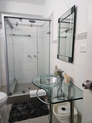 A bathroom with a glass shower enclosure, a glass sink, a toilet, and a mirror. - Fully Furnished Apartment in Miraflores (Miraflores)