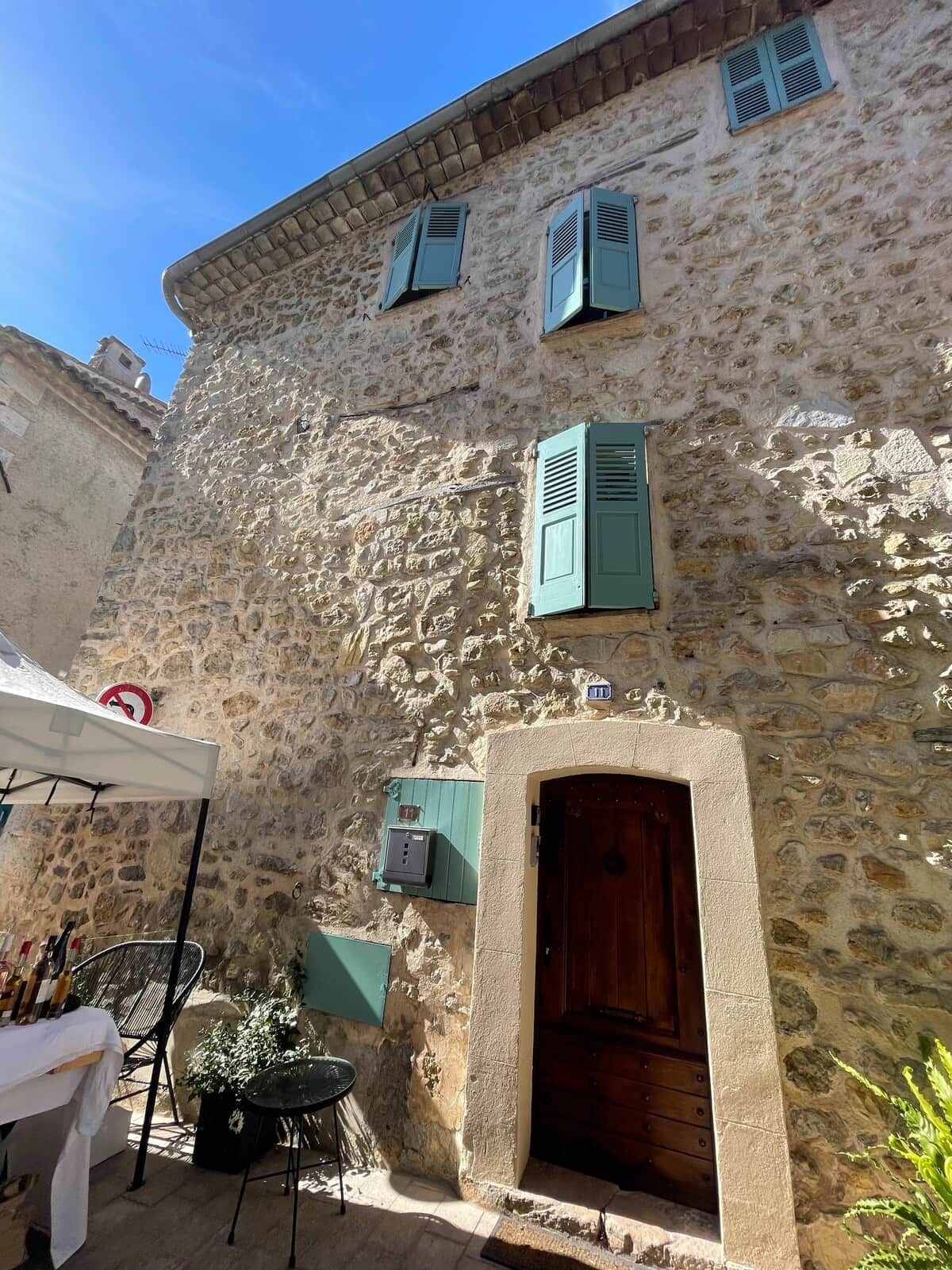 A stone building with a wooden door and shutters, outdoor seating, and a no parking sign.