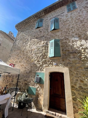 Un edificio in pietra con una porta e persiane di legno, sedute all'aperto e un segnale di divieto di parcheggio.