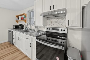 A modern kitchen with white cabinets, a stainless steel range hood, a double oven, and a granite countertop. - Oswego River View Work Hub Near Phoenix (Phoenix)