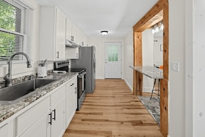 A kitchen with white cabinets, a granite countertop, a stainless steel sink, a built-in oven, and a refrigerator. - Oswego River View Work Hub Near Phoenix (Phoenix)