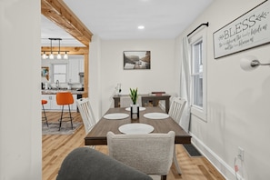 A dining area with a wooden table, white chairs, and a modern pendant light fixture. - Oswego River View Work Hub Near Phoenix (Phoenix)
