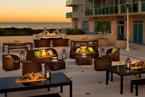 Eine Dachterrasse mit Außenmöbeln, einer Bar und Blick auf das Meer.