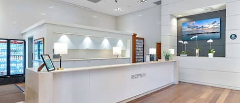 A reception desk with a 'RECEPTION' sign, a mounted TV screen, and a wall-mounted plant.