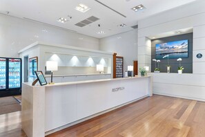 A reception desk with a 'RECEPTION' sign, a mounted TV screen, and a wall-mounted plant. - Bright & Stylish Room in Coconut Grove (Miami)