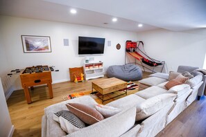 Ein Wohnzimmer mit einer Couch, einem Couchtisch, einem Kicker, einem Fernseher und einem kleinen Basketballkorb.