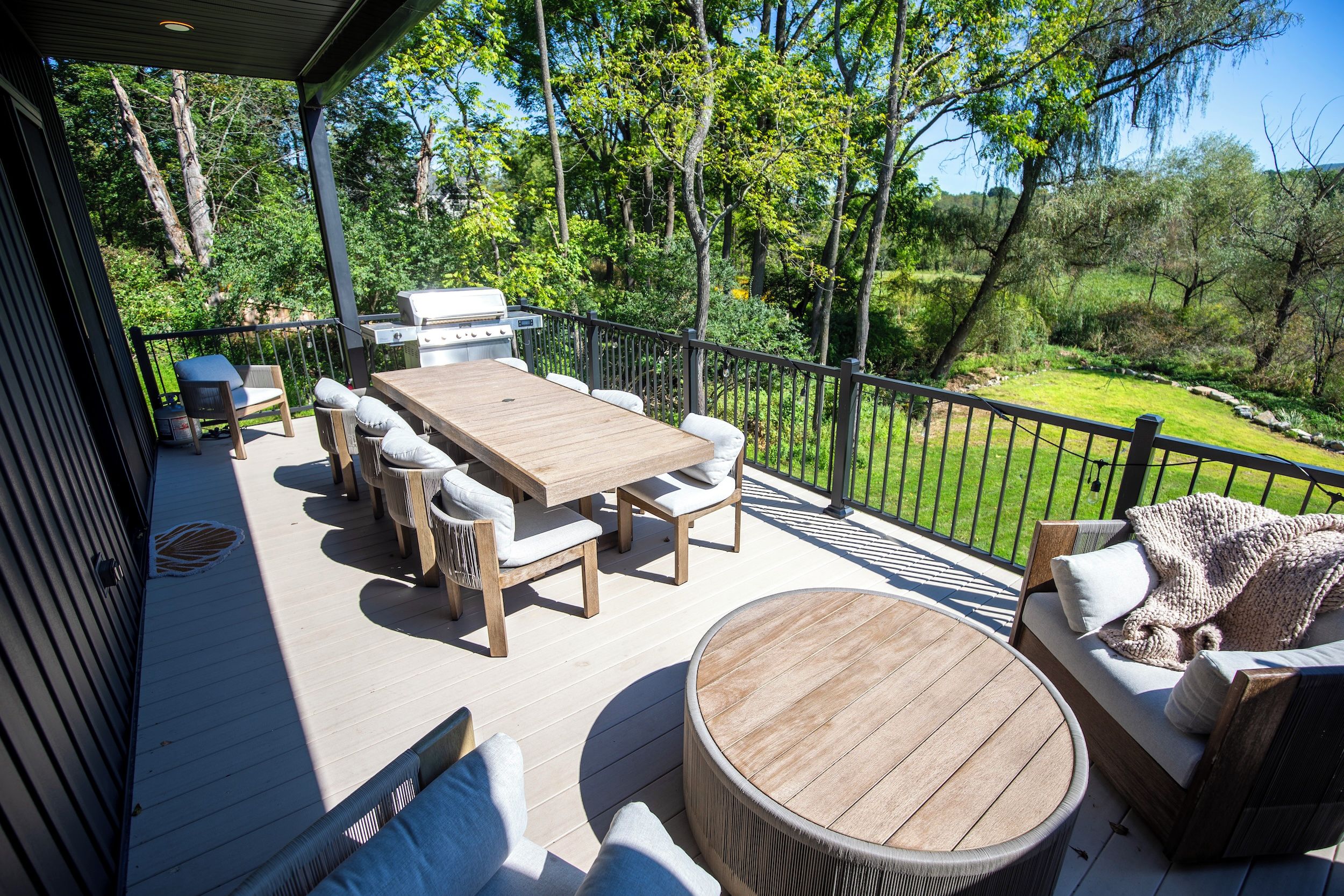 A covered outdoor deck with a dining table, chairs, and a grill.