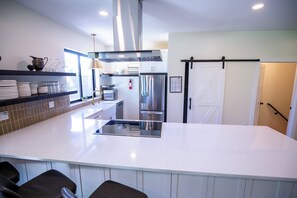 A modern kitchen with a central island, stainless steel appliances, and a sliding barn-style door. - Gameday Large Group Central 1 Mile From Stadium - Space for 16-19 (State College)