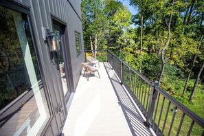 Ein Balkon mit Blick auf einen Wald, eine Glastür und zwei Korbstühle.