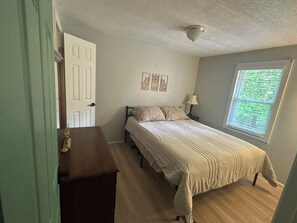 A bedroom with a bed, a nightstand, a lamp, a window with blinds, and a door. - Scenic Waterfront 1 Acre Home w/dock, kayaks, paddleboard, wifi and raised deck. (La Crosse)