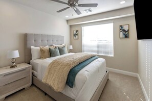 A bedroom with a bed, nightstand, lamp, ceiling fan, window with blinds, and two wall-mounted paintings. - Golden Gem with Views - Pool, PickleBall, 86" Smart TVs (Washington)