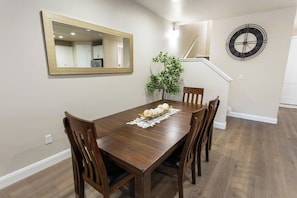 Un comedor con una mesa de madera, sillas, un espejo, un reloj y una escalera.