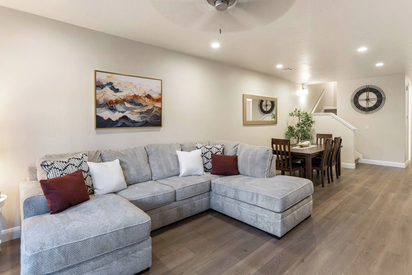 A living room with a grey sectional sofa, a dining table with chairs, a ceiling fan, and a painting on the wall.