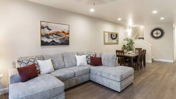 A living room with a grey sectional sofa, a dining table with chairs, a ceiling fan, and a painting on the wall.