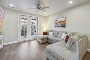 A living room with a sectional sofa, a ceiling fan, and a door leading to a balcony. - Golden Gem with Views - Pool, PickleBall, 86" Smart TVs (Washington)