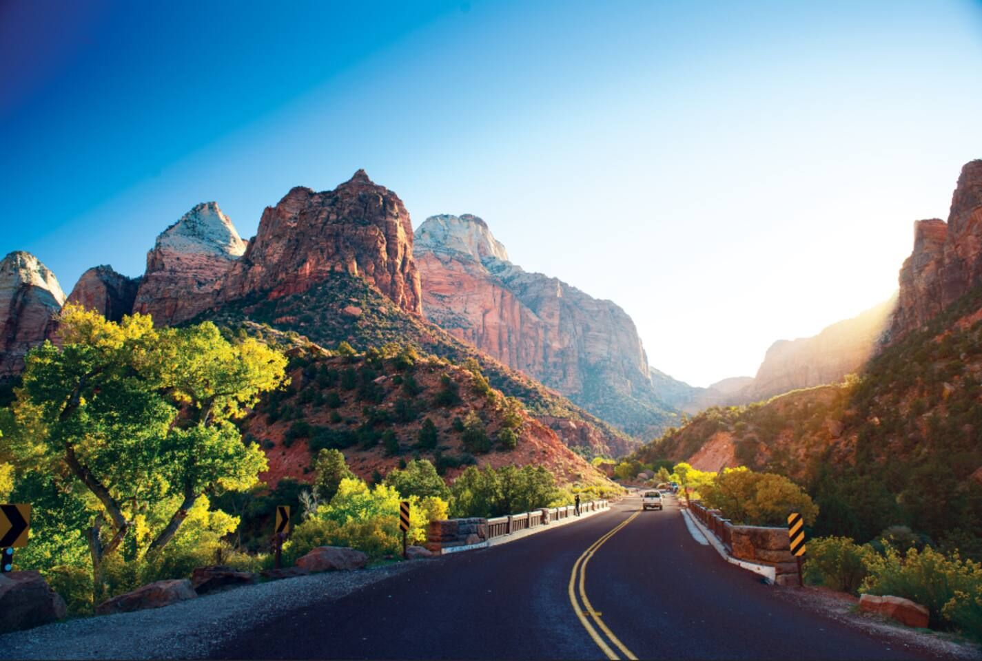 A road with guardrails, surrounded by rocky mountains and greenery.