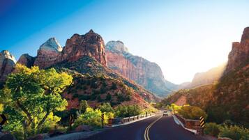 A road with guardrails, surrounded by rocky mountains and greenery.