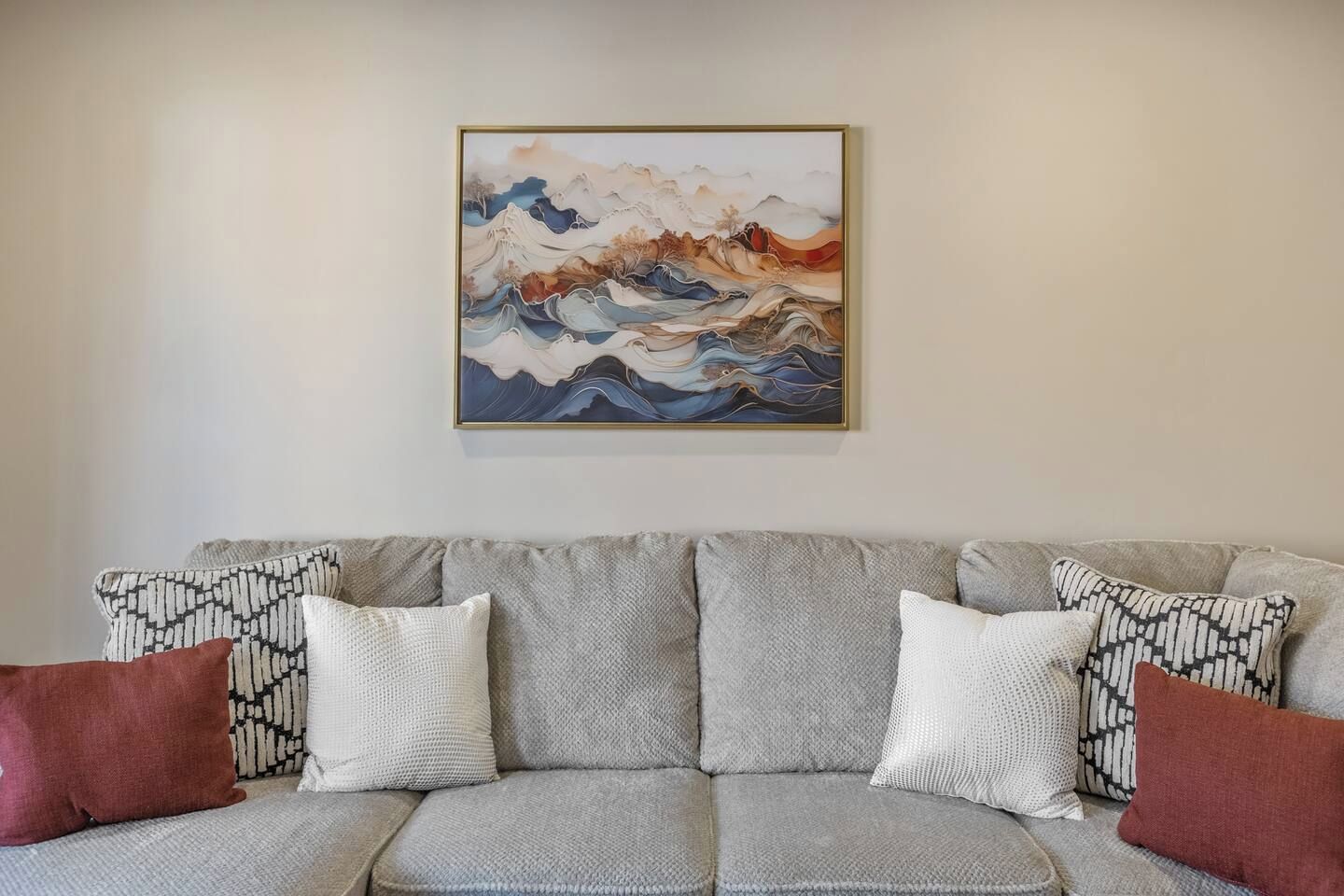 Una sala de estar con un sofá gris, cojines estampados y una obra de arte enmarcada en la pared.