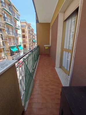 A balcony with a tiled floor, a metal railing, a window with a curtain, and a view of neighboring buildings. - Casa Mimosa - One Bedroom Apartment, Sleeps 5 (Marina di Andora)