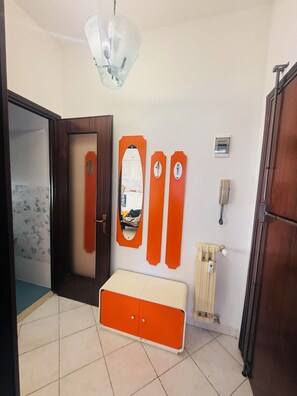 Una habitación con puerta, un banco, un radiador y una lámpara fijada a la pared.