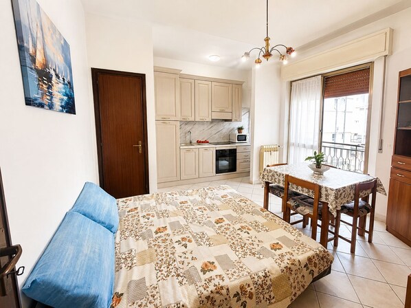 Een functionele leefruimte met een bed, een eettafel, een kitchenette en een balkon.