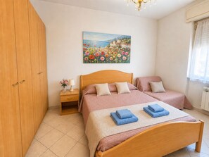 Un dormitorio con dos camas, un armario de madera, una mesita de noche con lámpara y un cuadro en la pared.