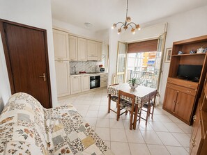 A compact kitchen with a dining area, a sofa, and a TV shelf. - Casa Mimosa - One Bedroom Apartment, Sleeps 5 (Marina di Andora)