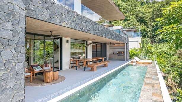 Una casa moderna con fachada de piedra, piscina y zona de estar exterior.