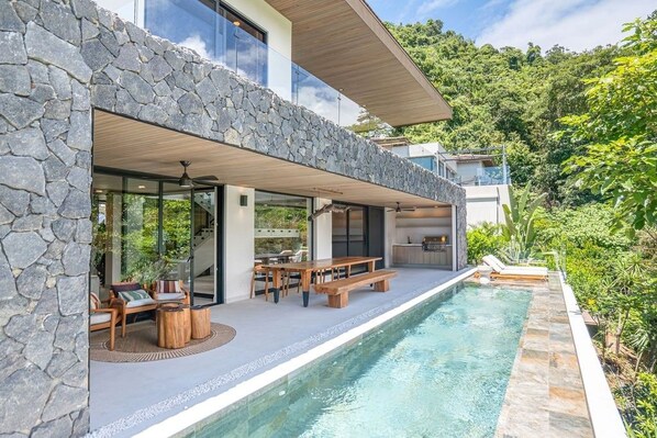 Een modern huis met een stenen gevel, een zwembad en terrasmeubels.