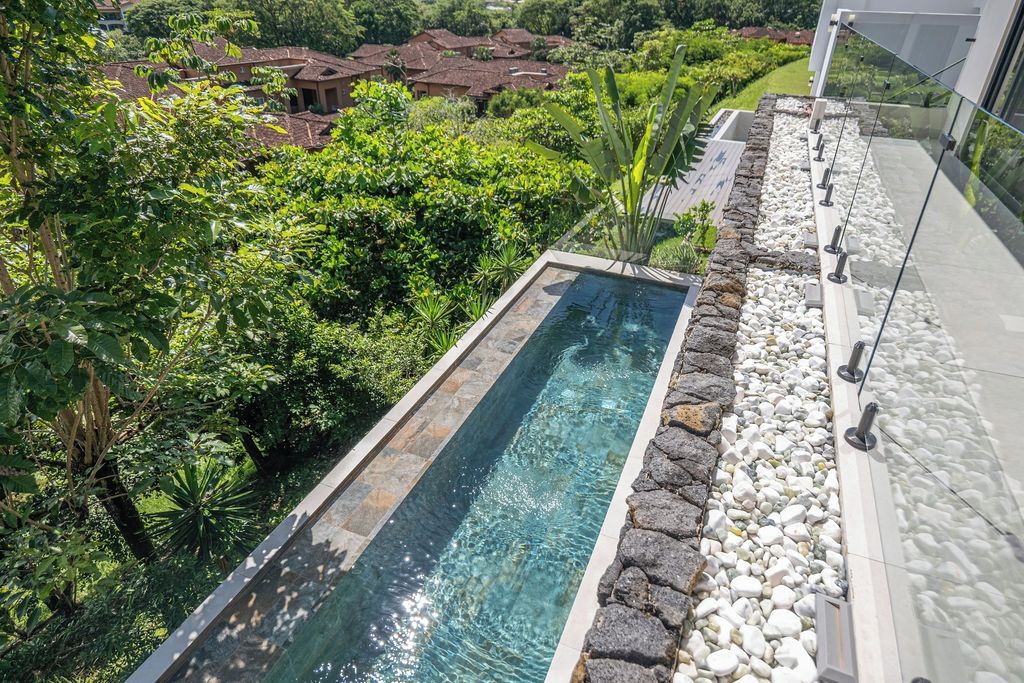 Ein rechteckiger Swimmingpool mit klarem Wasser, umgeben von einer Steinbordura und üppiger Bepflanzung.