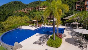 Un resort con piscina, sillas de descanso y montañas al fondo.