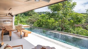 Zona de piscina moderna al aire libre con terraza de madera, asientos y vistas a exuberante vegetación.