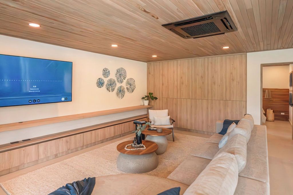 Ein modernes Wohnzimmer mit einem großen Flachbildfernseher an der Wand, einer Holzbalkendecke, einer Sitzecke mit Sofa und rundem Couchtisch sowie einem dekorativen Wandbild.