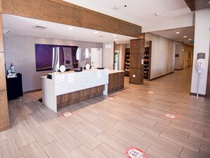 A reception area with a counter, a wall-mounted mirror, a poster, and a floor with social distancing markers.