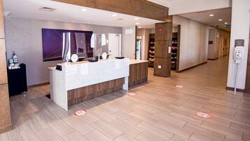 A reception area with a counter, a wall-mounted mirror, a poster, and a floor with social distancing markers.