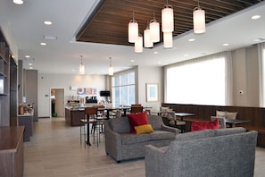Un hall d’hôtel moderne doté d’un bar, d’espaces aménagés pour s’asseoir et d’une grande fenêtre laissant entrer la lumière naturelle.