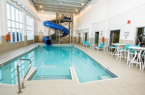 Una piscina interior con un tobogán azul, sillas de descanso y una estación de salvavidas.