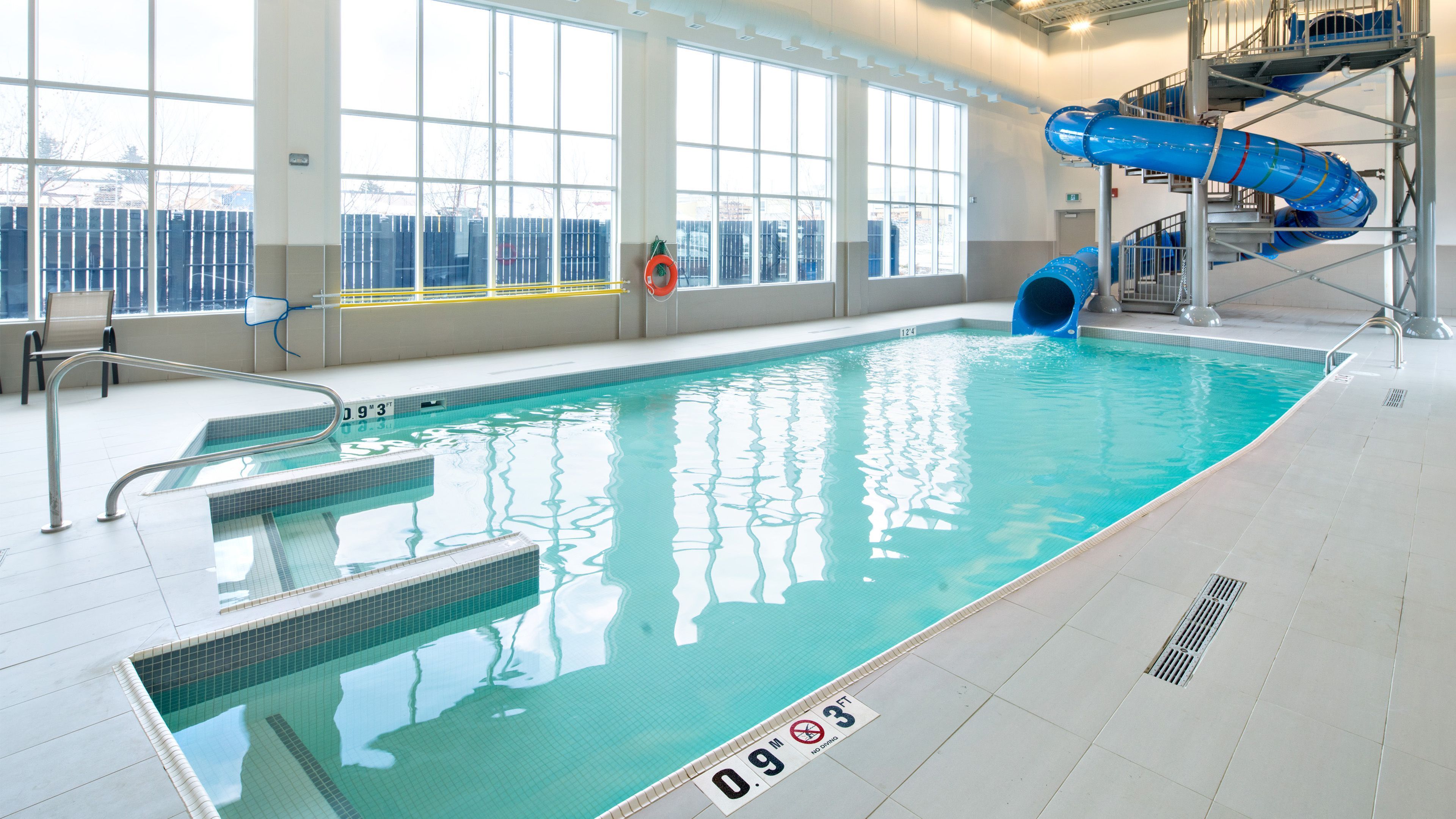 Una piscina interior con un tobogán azul, agua cristalina y marcas de profundidad de seguridad.